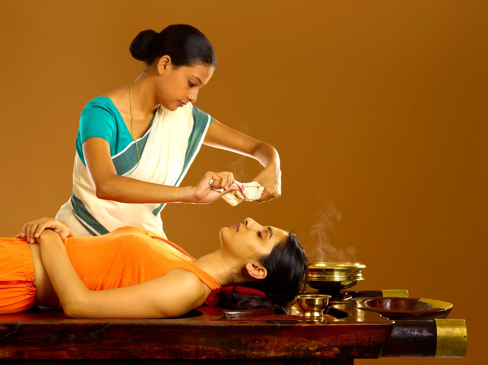 swedanam-practitioner holding steamed cloth near a lying lady